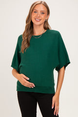 woman wearing a green oversized maternity sweater and holding her baby bump