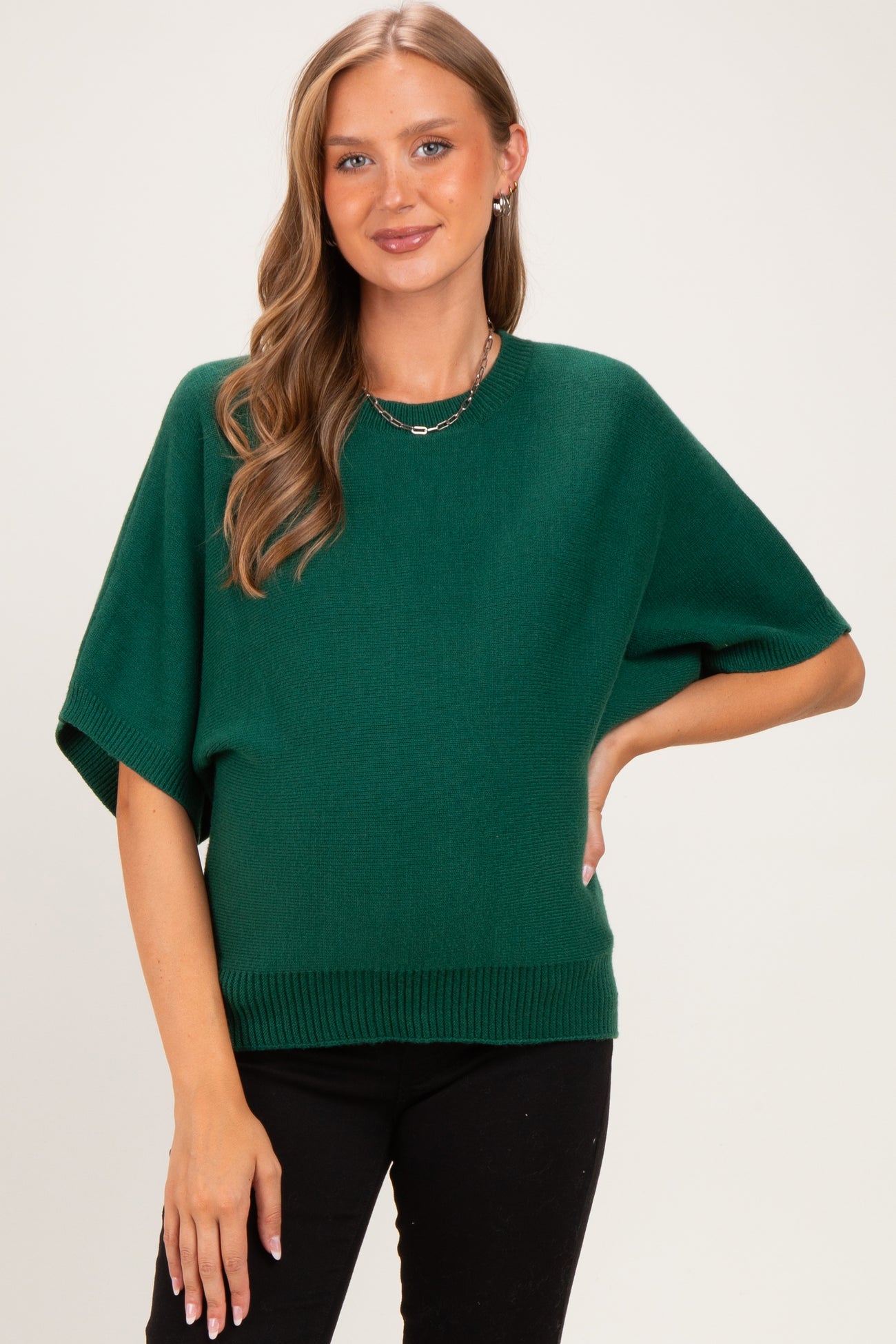 woman wearing a green short sleeve maternity sweater with a relaxed fit and ribbed hem, styled with black pants