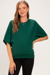 woman wearing a green short sleeve maternity sweater with a relaxed fit and ribbed hem, styled with black pants