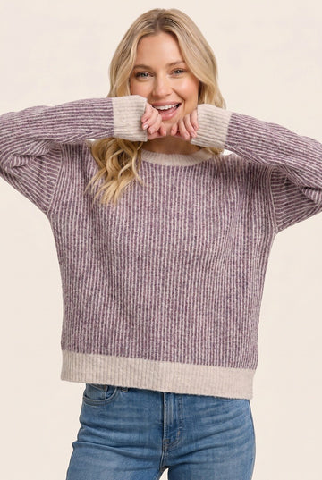 woman wearing a purple and cream striped oversized sweater and smiling with her hands near her face