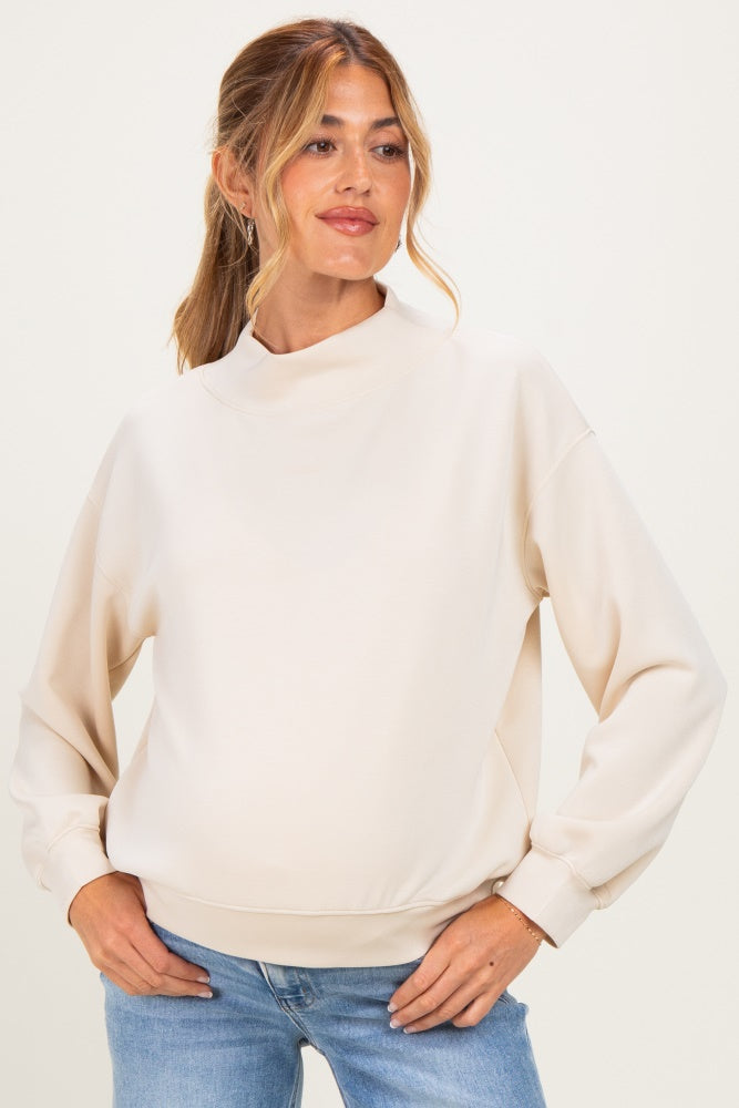 woman wearing a cream maternity sweatshirt with a high neck and balloon sleeves, showcasing her baby bump