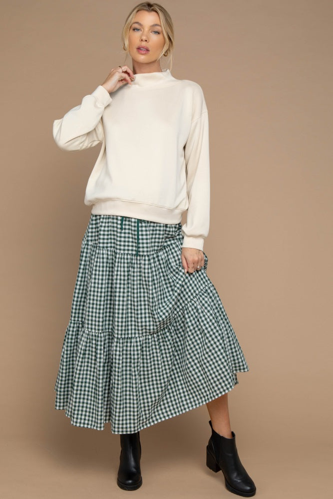 woman wearing a cream oversized sweatshirt and a green gingham tiered maxi skirt, styled with black ankle boots