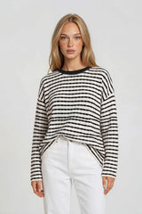 woman wearing a striped cream and black oversized sweater with a relaxed fit and long sleeves, paired with white pants