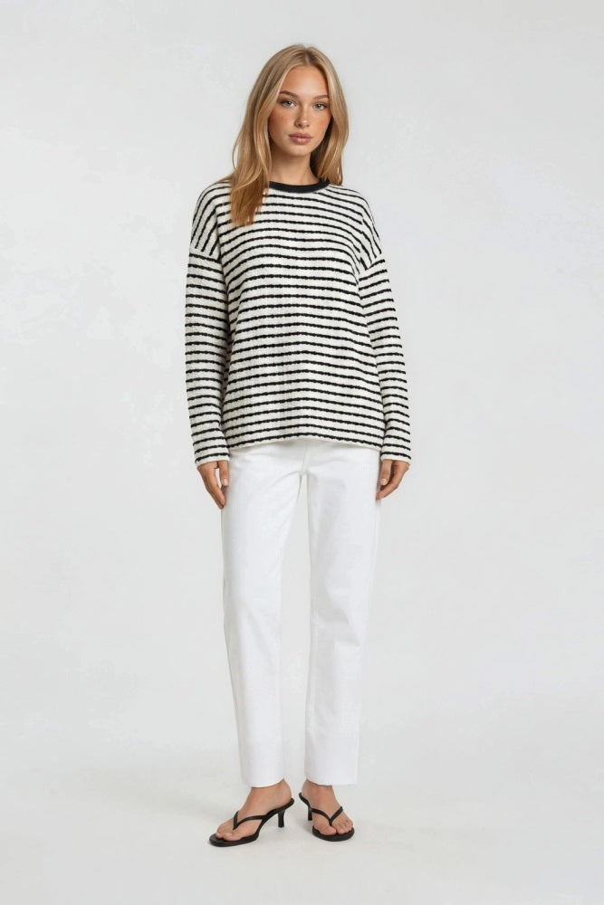 woman wearing a black and white striped sweater with long sleeves and white straight-leg pants