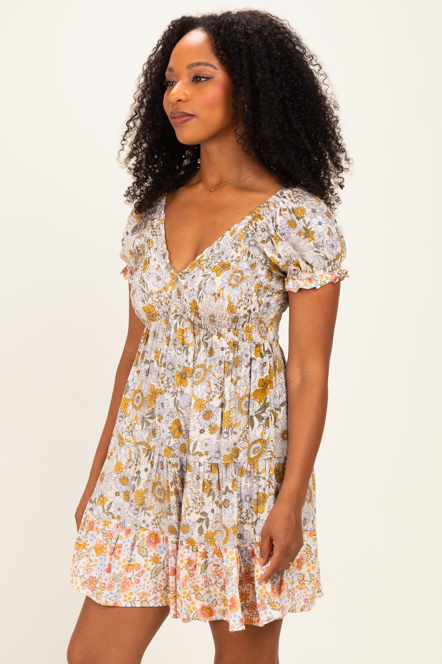 woman wearing a floral print short sleeve dress with a v-neck and ruched bodice in shades of yellow and orange