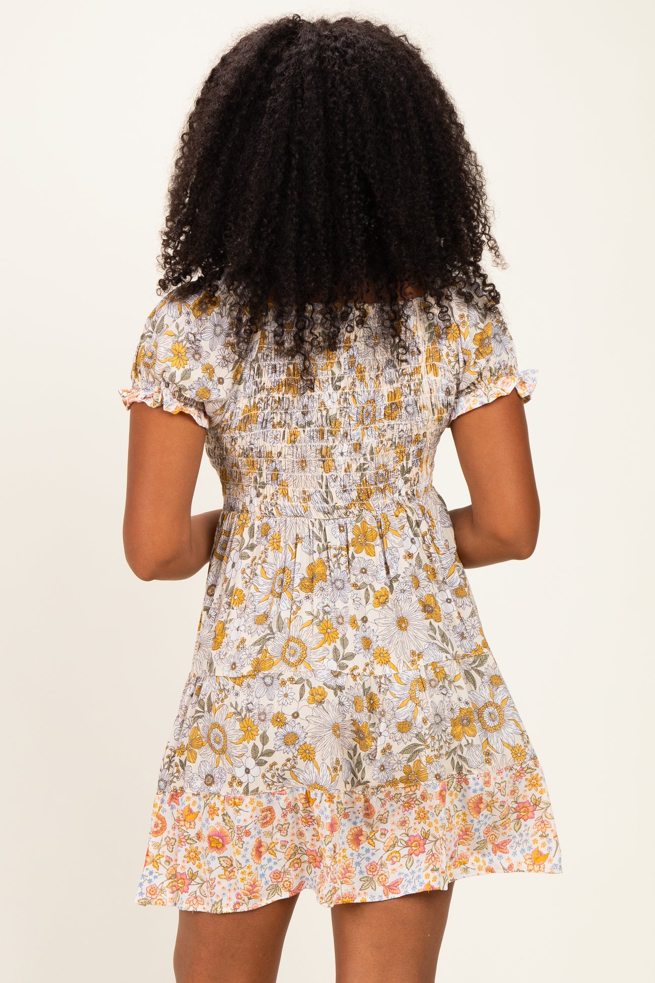 woman wearing a floral print short dress with a shirred bodice and ruffled sleeves, seen from the back