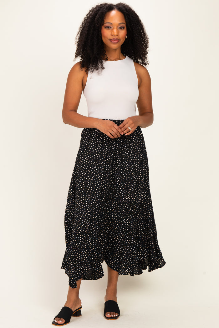 woman wearing a white sleeveless top and a black polka dot maxi skirt, standing confidently with hands clasped