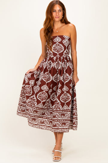 woman wearing a brown spaghetti strap maxi dress with white floral patterns and a tiered skirt