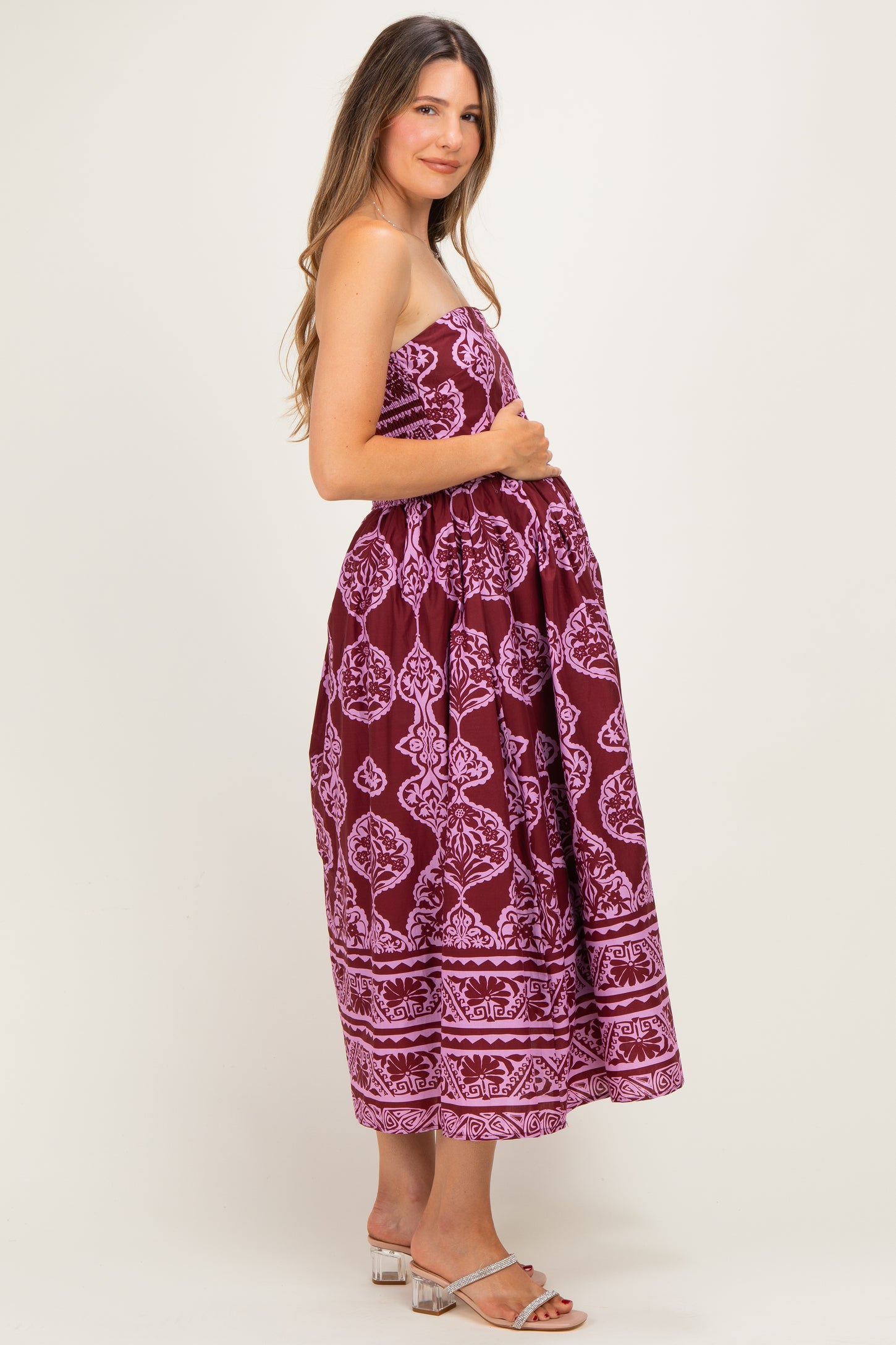 woman wearing a burgundy strapless maxi maternity dress with floral patterns and holding her baby bump