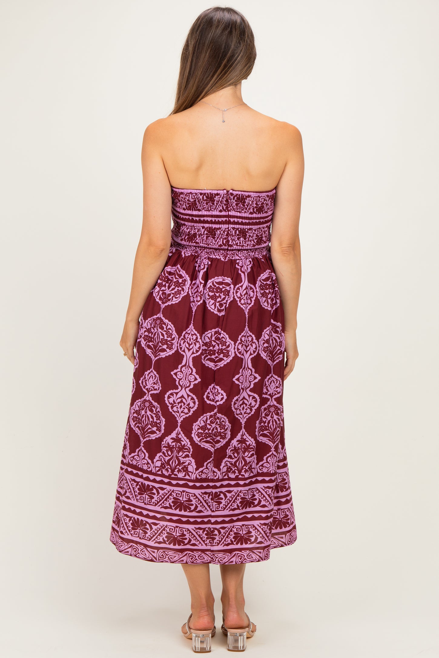 woman wearing a strapless burgundy maternity dress with white fabric pattern, showing her back and flowing mid-calf length