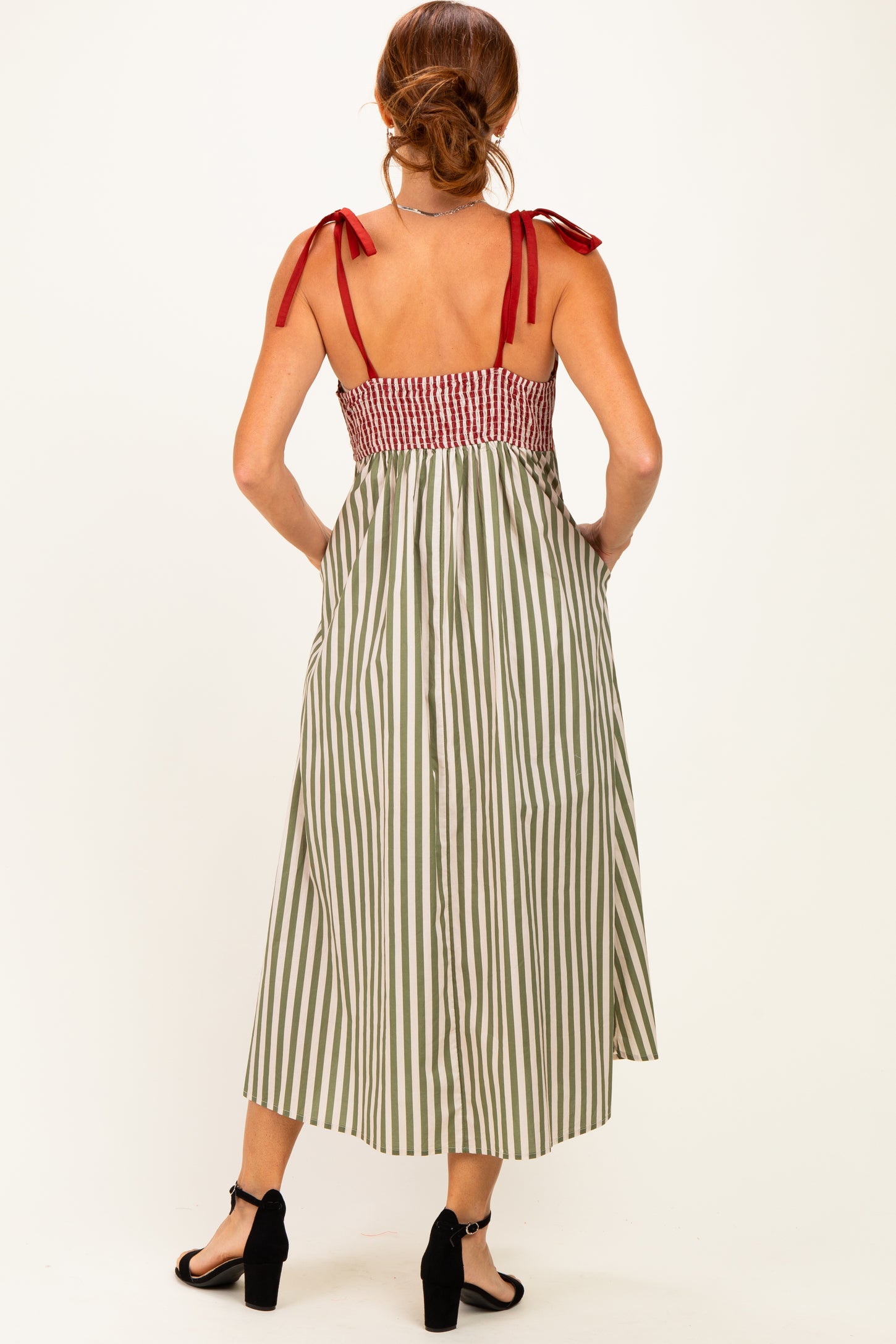 woman wearing a back view of a green and white striped maxi dress with red tie straps and smocked bodice