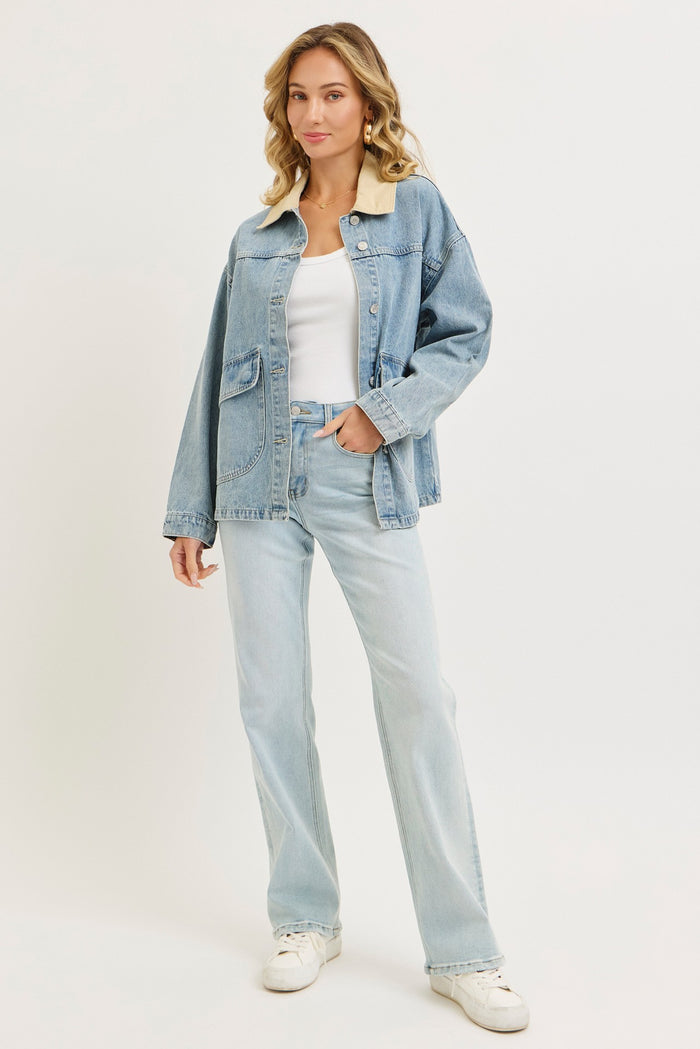 woman wearing a light blue denim jacket over a white tank top and light blue flared jeans with white sneakers