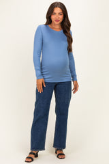 woman wearing a light blue long sleeve maternity top and dark denim jeans, showcasing her baby bump