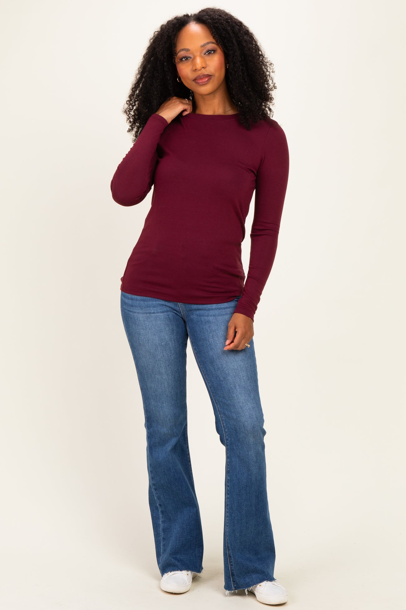 woman wearing a burgundy long sleeve top paired with light blue flared jeans and white sneakers