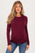woman wearing a burgundy long sleeve maternity top with a visible baby bump and blue jeans