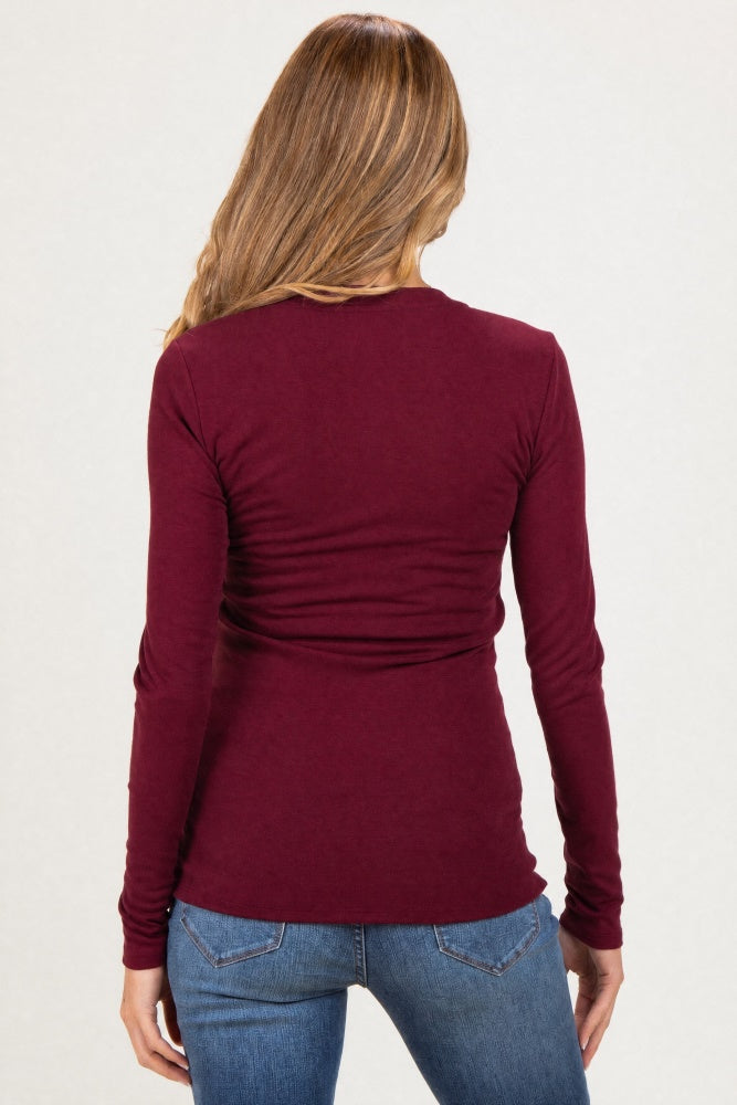 woman wearing a burgundy long sleeve maternity top with a ruched back detail and blue jeans