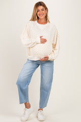 woman wearing a cream maternity sweater with floral print and holding her baby bump, paired with light blue jeans