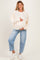 woman wearing a cream maternity sweater with floral print and holding her baby bump, paired with light blue jeans
