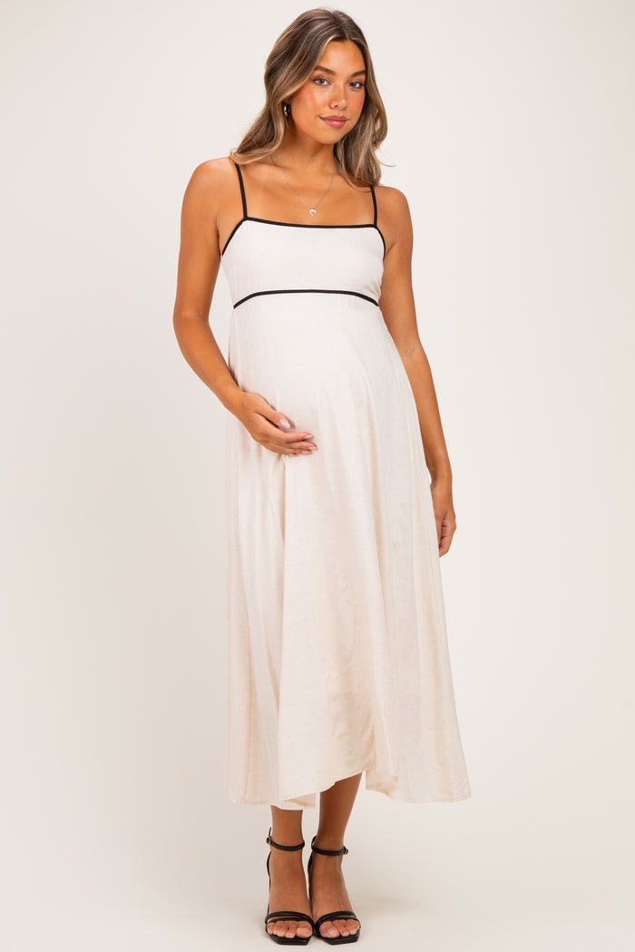 woman wearing a beige maternity dress with black trim, posing with her baby bump visible