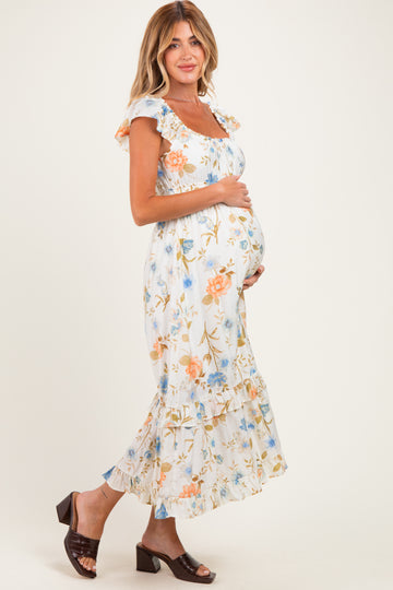 woman wearing a floral white maternity dress with ruffled sleeves, cradling a visible baby bump