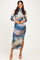 woman wearing a long sleeve fitted maxi dress with a blue and beige abstract pattern and a thigh-high slit