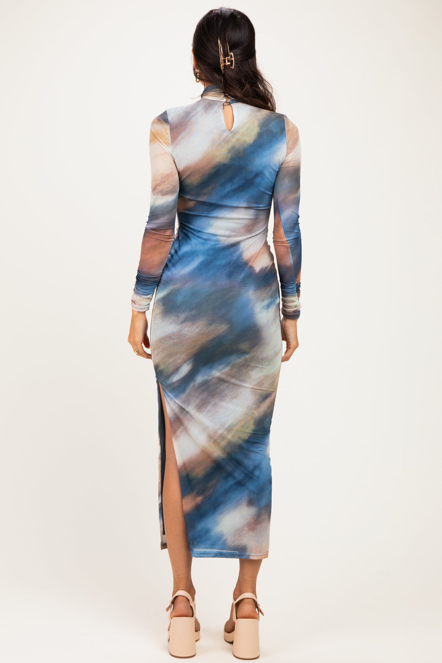 woman wearing a long sleeve blue and multicolor abstract patterned dress with a side slit and keyhole back detail