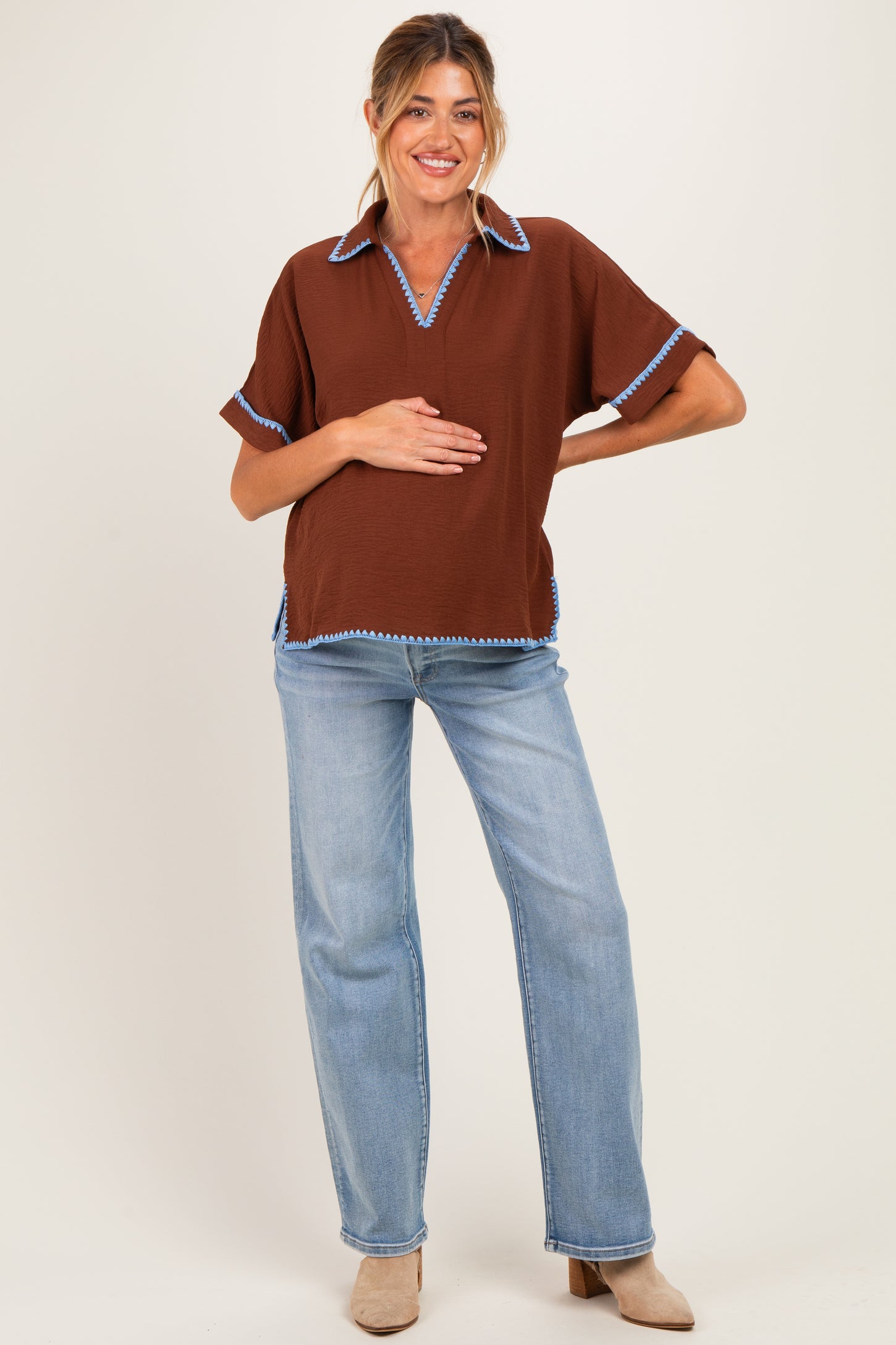 woman wearing a brown maternity top with blue trim and jeans, holding her baby bump