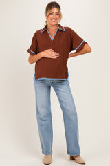 woman wearing a brown maternity top with blue trim and jeans, holding her baby bump