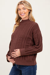 woman wearing a brown cable knit maternity sweater and holding her baby bump