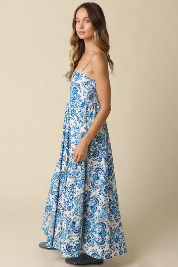 woman wearing a floral blue and white maxi dress with thin straps and a tiered skirt
