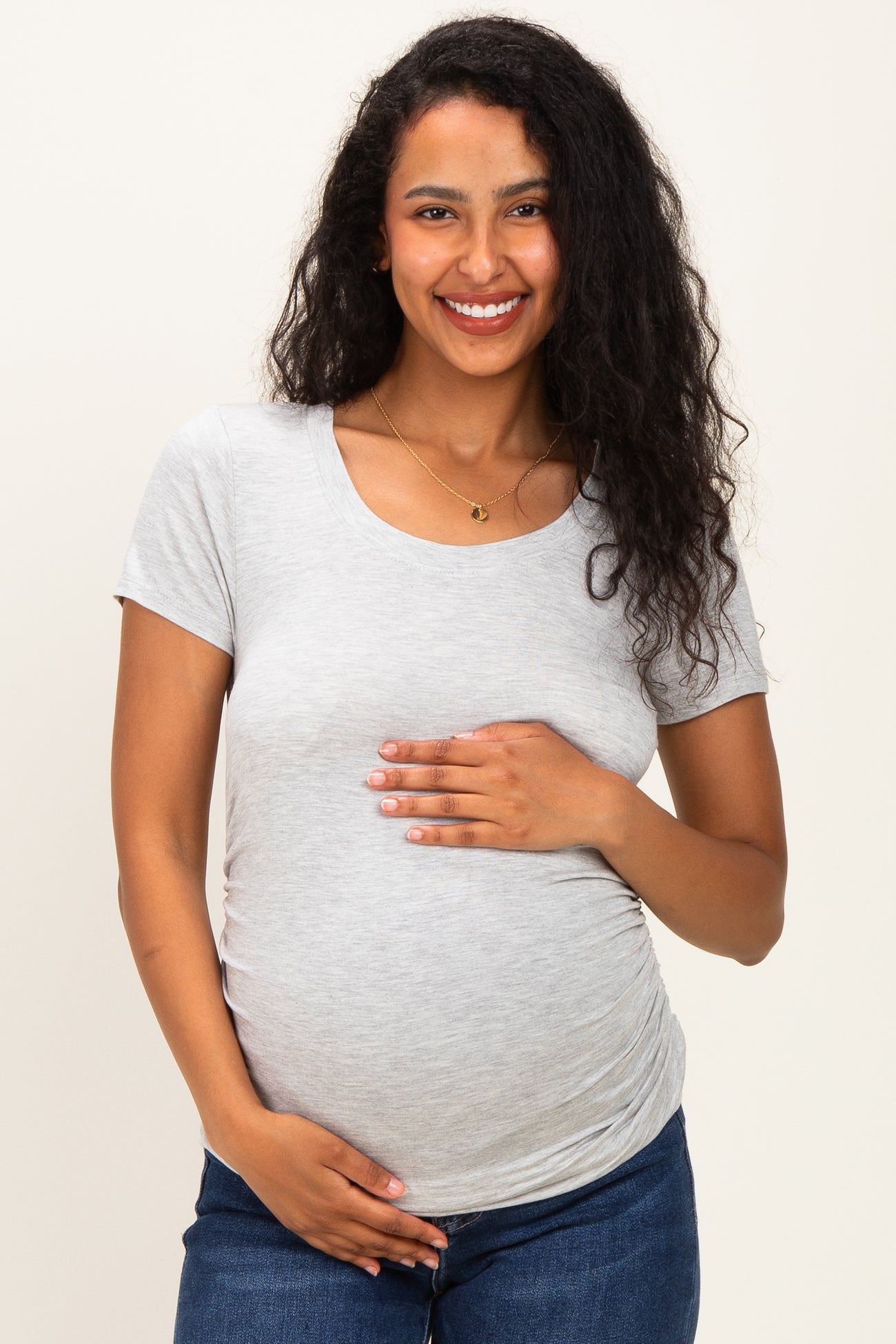 woman wearing a light grey short sleeve maternity top and holding her baby bump