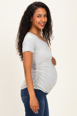 woman wearing a gray short sleeve maternity top with side ruching and displaying her baby bump