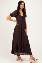 woman wearing a dark brown lace maxi dress with puff sleeves and a tiered skirt, posing with a smile