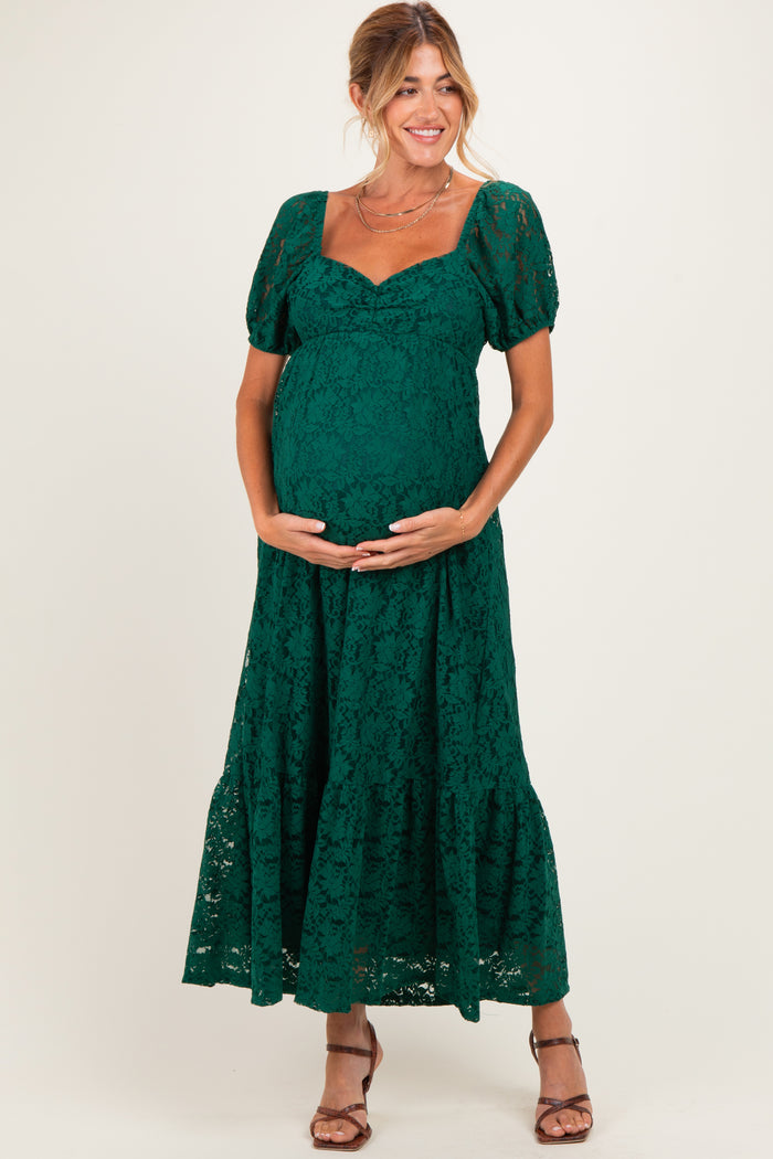 woman wearing a dark green lace maternity dress with puff sleeves and a flowing skirt, holding her baby bump