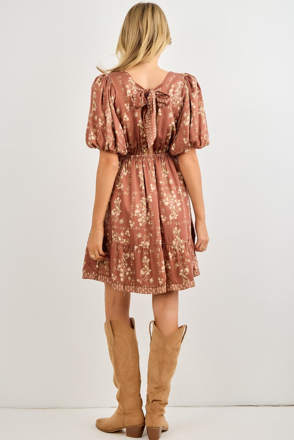 woman wearing a rust-colored floral puff sleeve dress with a bow detail at the back and a tiered skirt