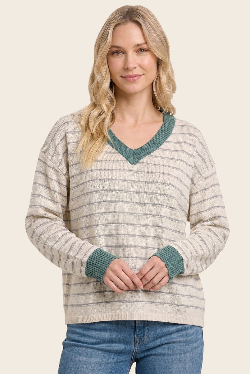 woman wearing a cream striped sweater with a v-neck and teal trim, styled with blue jeans