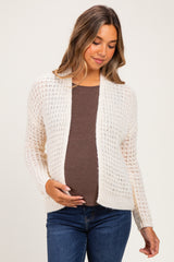 woman wearing a light beige maternity cardigan over a brown top and holding her baby bump
