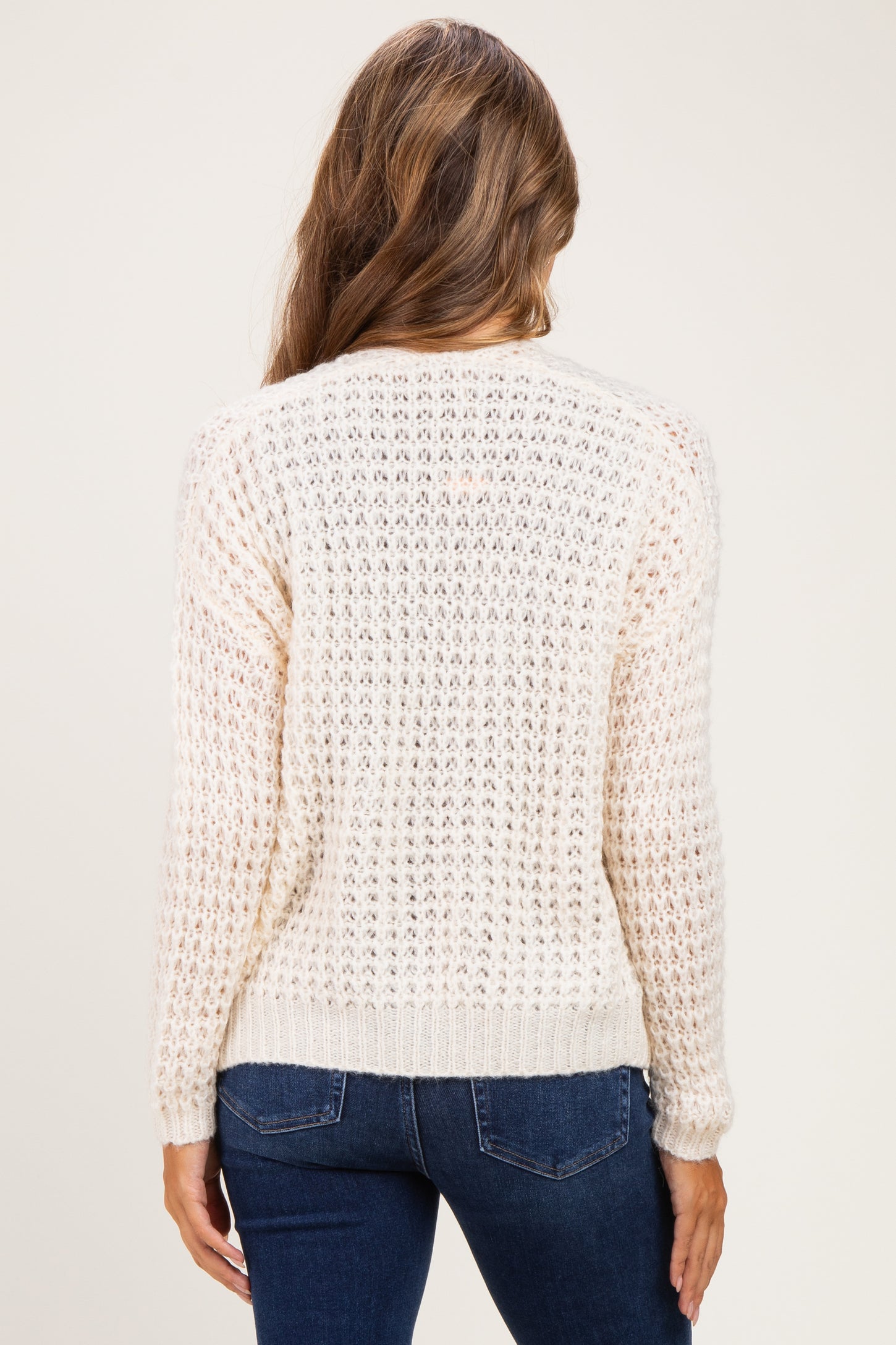 woman wearing a cream-colored open-knit maternity sweater with a relaxed fit and long sleeves