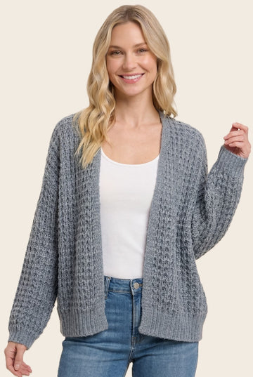 woman wearing a gray chunky knit cardigan over a white top paired with blue jeans and smiling