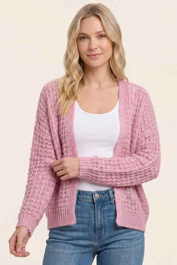 woman wearing a light pink textured cardigan over a white top and blue jeans