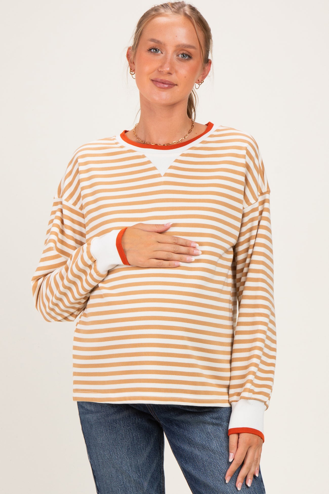 woman wearing a striped maternity top in beige and white with orange accents, holding her baby bump