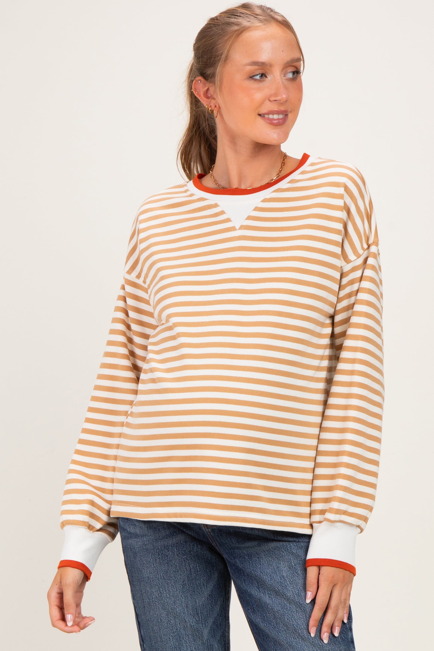 woman wearing a striped maternity sweatshirt in beige and white with red accents, styled with jeans and a baby bump visible