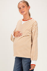 woman wearing a striped beige and white maternity top with orange accents, holding her baby bump
