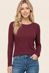 woman wearing a burgundy long sleeve ribbed top with a round neckline, paired with blue jeans