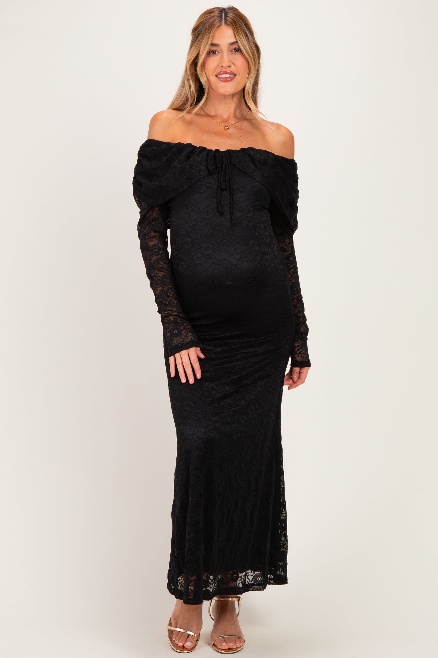 woman wearing a black off-the-shoulder lace maternity dress with long sleeves and a fitted silhouette, showing her baby bump