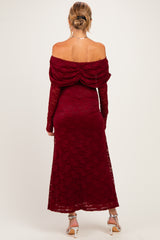 woman wearing a burgundy off-the-shoulder maternity dress with long sleeves and lace detailing, showing her baby bump