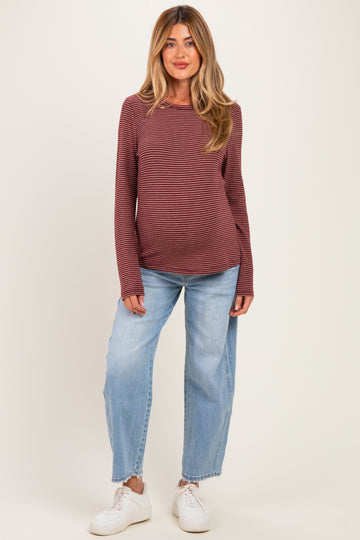 woman wearing a burgundy striped long sleeve maternity top and light blue wide-leg jeans, showing her baby bump
