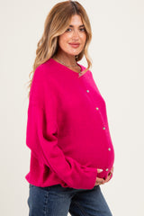 woman wearing a fuchsia maternity sweater with buttons, highlighting her baby bump while smiling at the camera