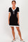 woman wearing a black ribbed short sleeve dress with white ruffle trim and a tie detail at the neckline