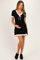woman wearing a black maternity dress with white trim and a bow, holding her baby bump